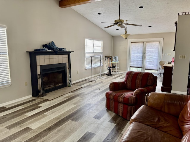 living area featuring vaulted ceiling with beams, a textured ceiling, a tile fireplace, wood finished floors, and baseboards