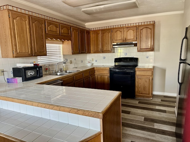 kitchen with tile countertops, a peninsula, under cabinet range hood, black appliances, and a sink