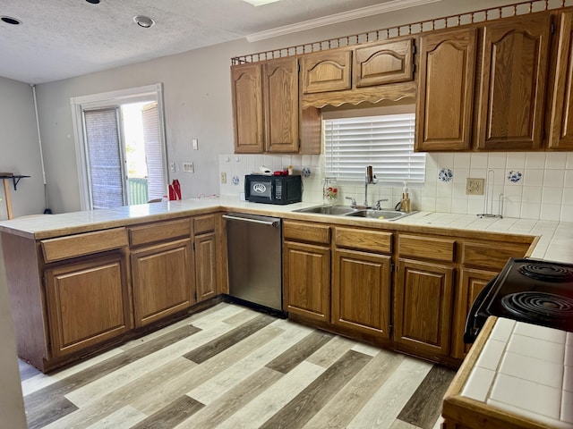 kitchen featuring tile countertops, a peninsula, stainless steel dishwasher, and a sink