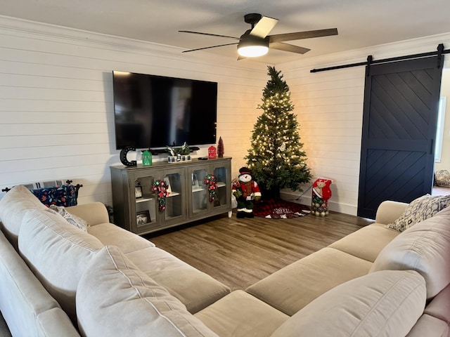 living room featuring dark wood-style floors, a barn door, ornamental molding, and a ceiling fan