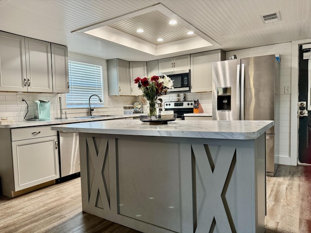 kitchen featuring gray cabinetry, stainless steel appliances, a raised ceiling, and a center island