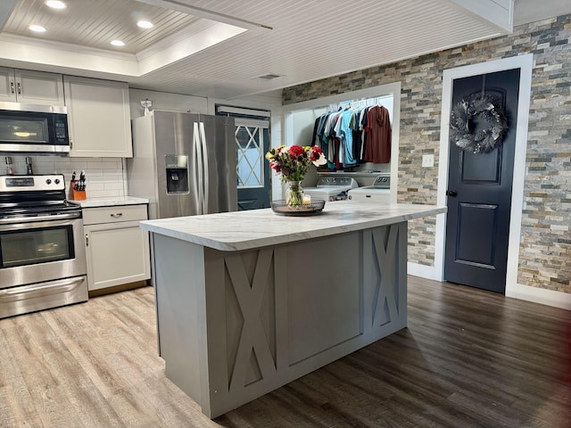 kitchen featuring stainless steel appliances, a tray ceiling, light wood-style floors, and separate washer and dryer