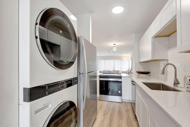 washroom featuring stacked washing maching and dryer, sink, and light hardwood / wood-style flooring