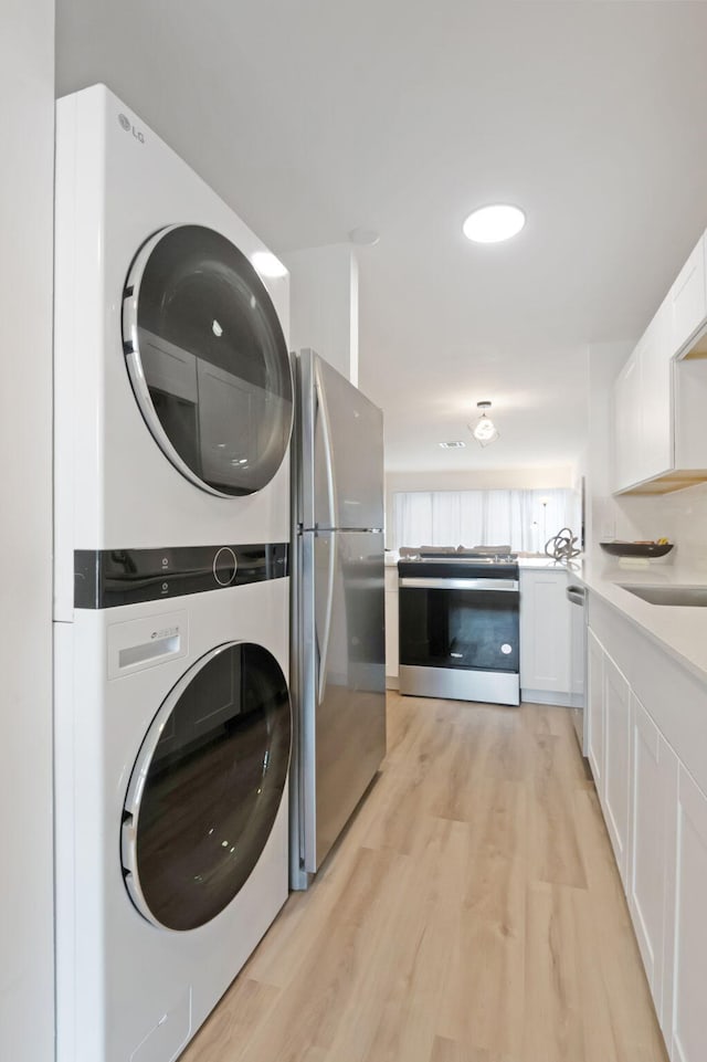 washroom with light hardwood / wood-style flooring, stacked washer / drying machine, and sink