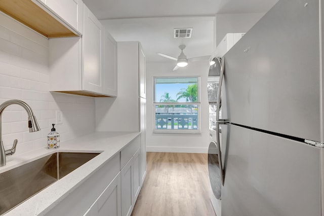 kitchen with decorative backsplash, stainless steel fridge, white cabinetry, and sink