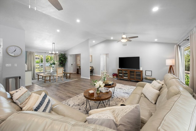 living room with plenty of natural light, ceiling fan with notable chandelier, vaulted ceiling, and light wood-type flooring