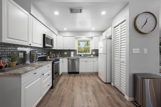 kitchen with white cabinets, light hardwood / wood-style floors, stone countertops, and appliances with stainless steel finishes