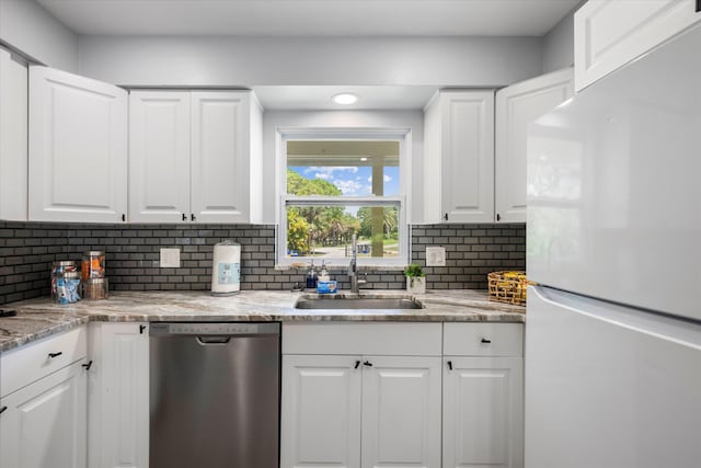 kitchen featuring white refrigerator, sink, stainless steel dishwasher, decorative backsplash, and white cabinetry