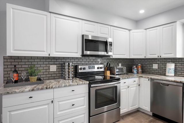 kitchen with backsplash, dark wood-type flooring, white cabinets, light stone countertops, and appliances with stainless steel finishes