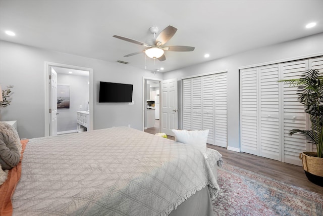 bedroom featuring hardwood / wood-style floors, ensuite bathroom, two closets, and ceiling fan