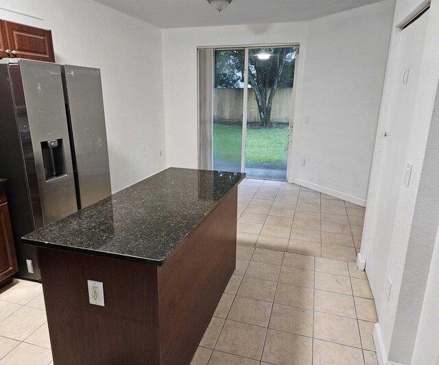 kitchen featuring light tile patterned flooring, dark stone countertops, dark brown cabinets, a kitchen island, and stainless steel fridge with ice dispenser