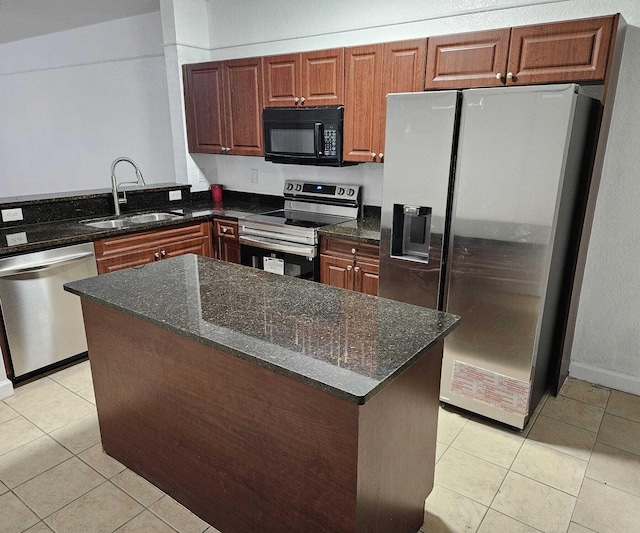 kitchen featuring appliances with stainless steel finishes, sink, light tile patterned floors, dark stone countertops, and a center island