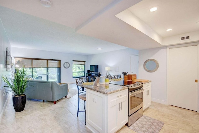 kitchen with light stone countertops, stainless steel electric stove, white cabinetry, a kitchen island, and a breakfast bar area