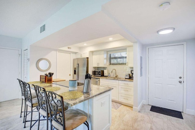 kitchen featuring light stone counters, backsplash, a breakfast bar, white cabinets, and appliances with stainless steel finishes