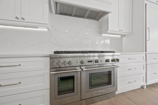 kitchen with exhaust hood, range with two ovens, light hardwood / wood-style flooring, decorative backsplash, and white cabinetry