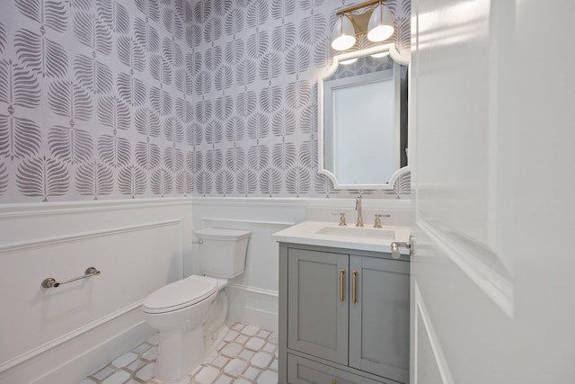 half bath featuring toilet, wainscoting, vanity, and a decorative wall