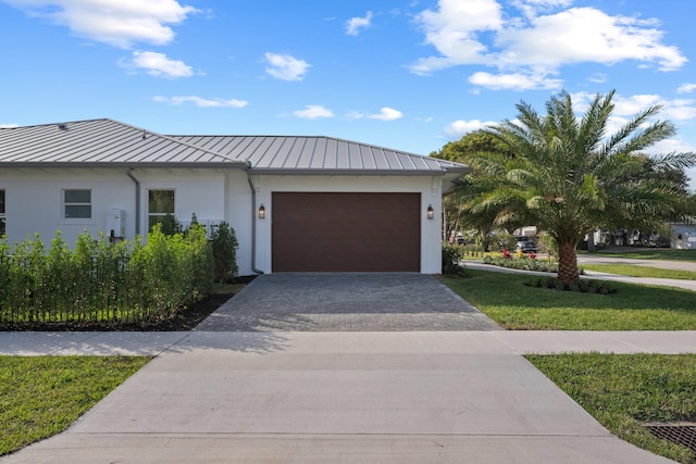 view of front facade with metal roof, an attached garage, decorative driveway, stucco siding, and a standing seam roof