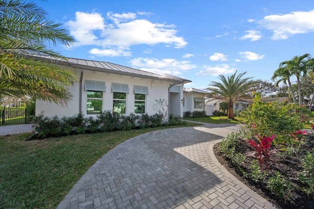 view of front of home featuring metal roof, decorative driveway, stucco siding, a front lawn, and a standing seam roof