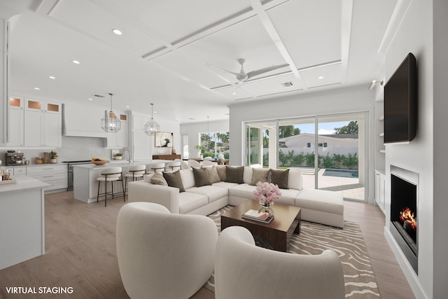 living room featuring a warm lit fireplace, coffered ceiling, ceiling fan, light wood-style floors, and recessed lighting