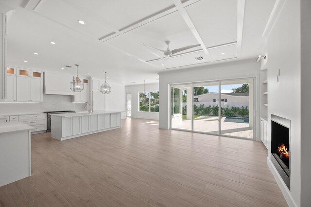 living room with a wealth of natural light, ceiling fan, light hardwood / wood-style floors, and coffered ceiling