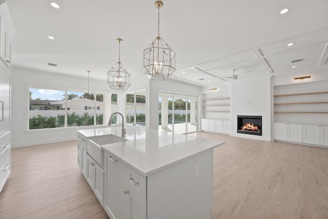 kitchen with an island with sink, white cabinetry, pendant lighting, and a sink