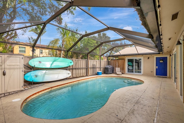 view of pool with glass enclosure, a grill, and a patio area