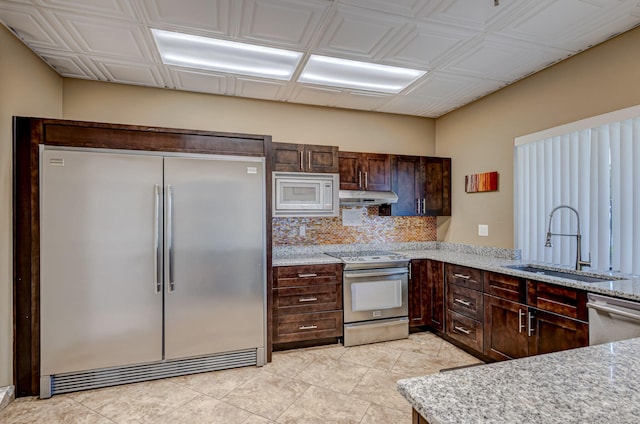 kitchen with built in appliances, light stone countertops, sink, and light tile patterned flooring