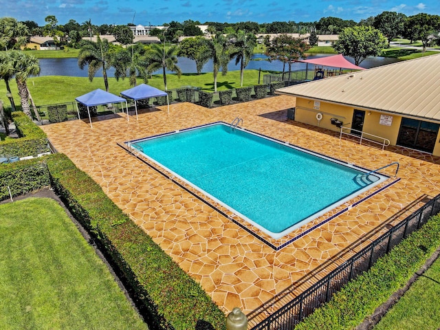 view of swimming pool featuring a patio area, a water view, and a yard