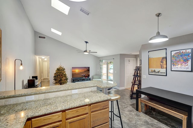 kitchen with ceiling fan, a kitchen breakfast bar, light stone counters, lofted ceiling with skylight, and decorative light fixtures