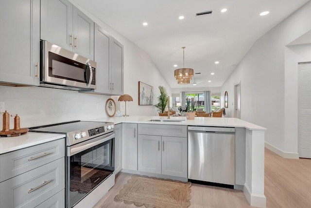 kitchen with kitchen peninsula, light wood-type flooring, lofted ceiling, and appliances with stainless steel finishes