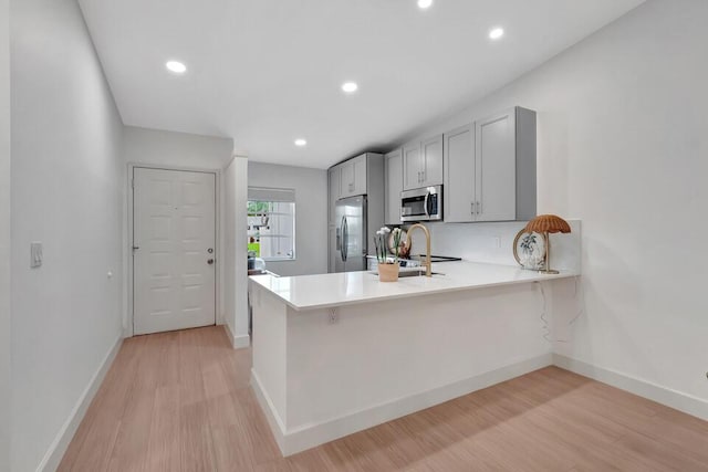 kitchen featuring kitchen peninsula, appliances with stainless steel finishes, light hardwood / wood-style floors, and gray cabinetry