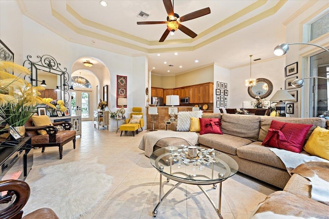 living room with a high ceiling, a tray ceiling, ceiling fan, and ornamental molding