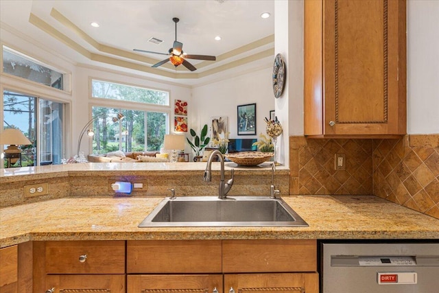 kitchen with ceiling fan, sink, a raised ceiling, stainless steel dishwasher, and backsplash