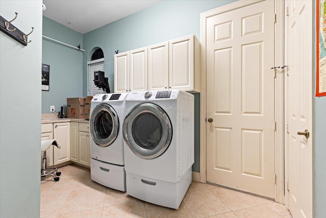 clothes washing area with cabinets, light tile patterned floors, and washing machine and clothes dryer