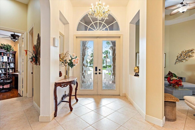 tiled entryway featuring ceiling fan with notable chandelier, a high ceiling, and french doors