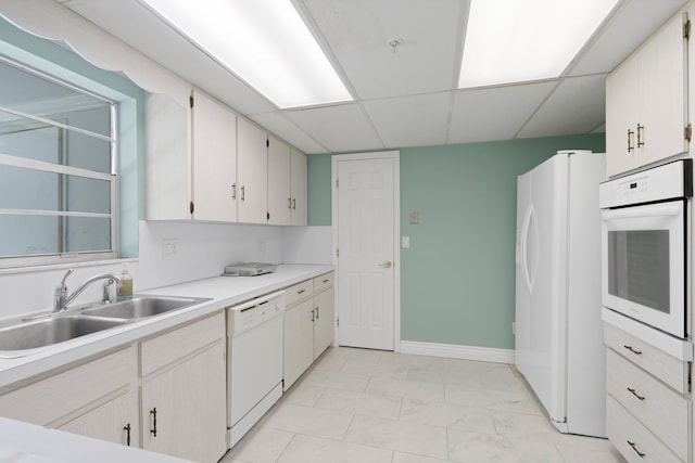 kitchen with a paneled ceiling, white appliances, white cabinets, sink, and light tile patterned floors