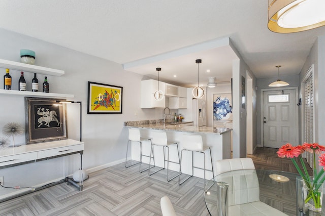 kitchen with white cabinetry, a kitchen bar, kitchen peninsula, hanging light fixtures, and light stone counters