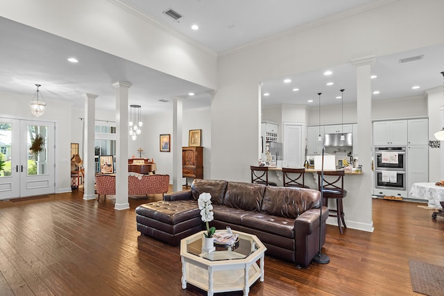 living room featuring ornate columns, a chandelier, dark hardwood / wood-style floors, and ornamental molding