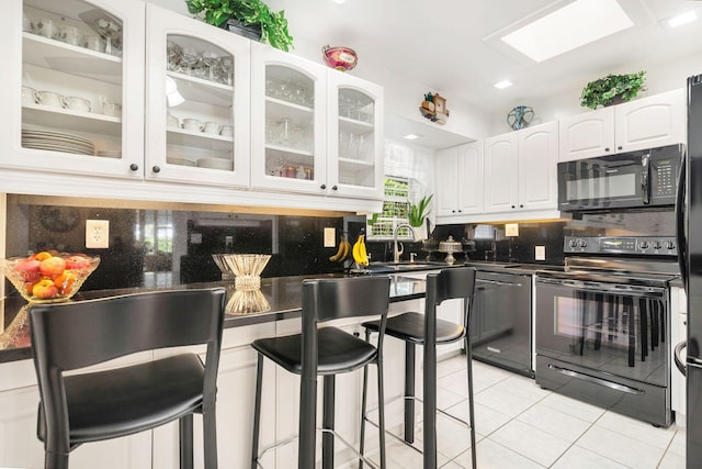 kitchen with backsplash, white cabinetry, a breakfast bar area, and black appliances