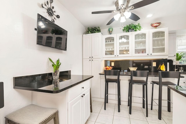 kitchen with a kitchen bar, backsplash, white cabinetry, and light tile patterned flooring