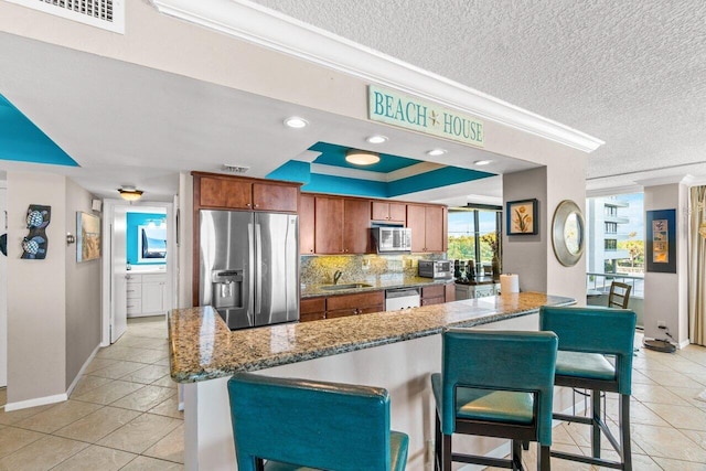 kitchen featuring appliances with stainless steel finishes, light stone counters, crown molding, sink, and a breakfast bar area