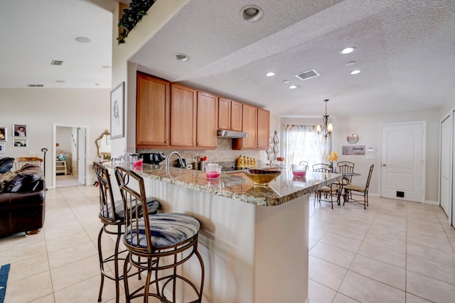 kitchen featuring kitchen peninsula, light stone countertops, hanging light fixtures, and a textured ceiling