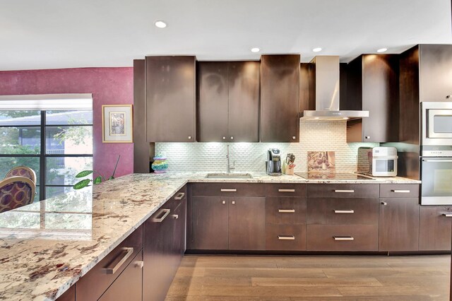 kitchen with light stone countertops, wall chimney range hood, sink, and light hardwood / wood-style flooring