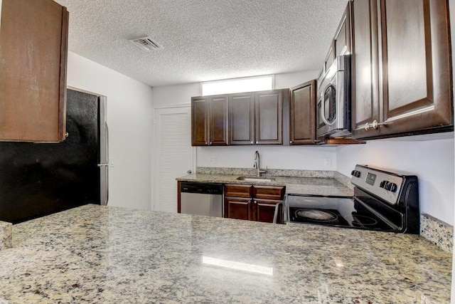 kitchen featuring light stone counters, a textured ceiling, dark brown cabinetry, stainless steel appliances, and sink