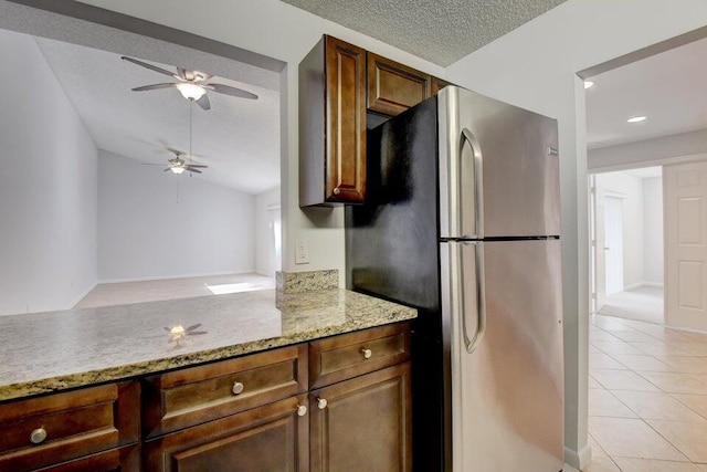 kitchen with ceiling fan, light tile patterned floors, a textured ceiling, light stone counters, and stainless steel refrigerator