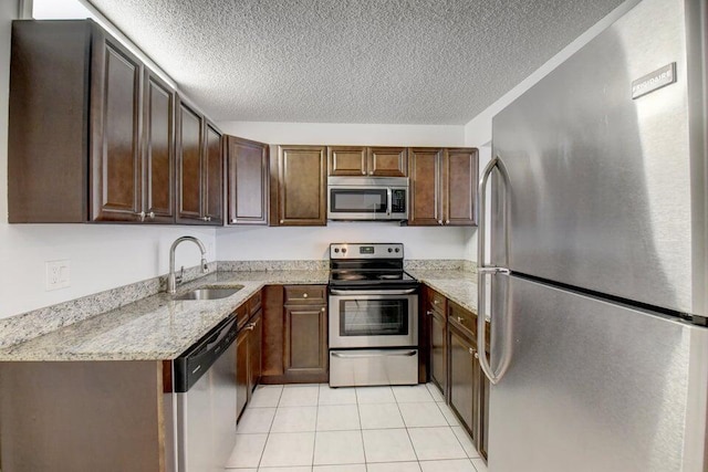 kitchen featuring sink, light tile patterned floors, a textured ceiling, light stone counters, and stainless steel appliances