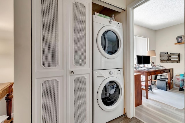 laundry room with a textured ceiling, light hardwood / wood-style floors, and stacked washer and clothes dryer