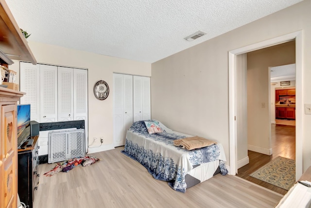 bedroom with light wood-type flooring, a textured ceiling, and two closets