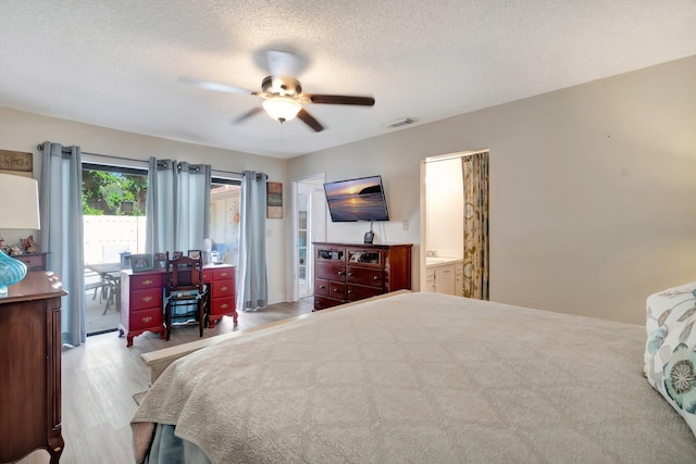 bedroom with ceiling fan, light wood-type flooring, a textured ceiling, and connected bathroom