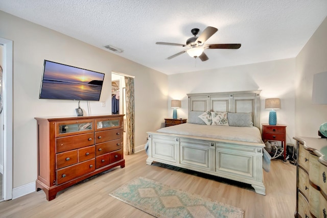 bedroom featuring a walk in closet, ceiling fan, light hardwood / wood-style flooring, and a textured ceiling